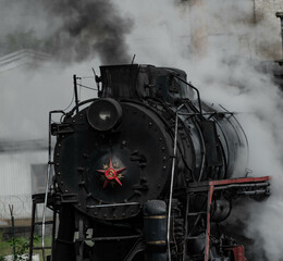 Naklejka premium an old vintage steam locomotive in close-up with a red star on the nose covered in huge clouds of steam and smoke