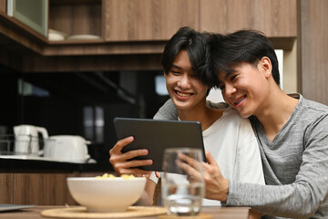 Asian LGBT couple having an enjoy moment with their digital tablet with kitchen as the background, LGBT couple lifestyle, Relationships and Equality concept.