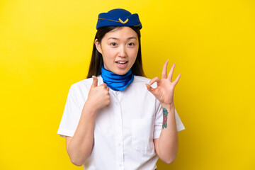 Airplane Chinese woman stewardess isolated on yellow background showing ok sign and thumb up gesture