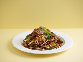 wok-fried Hor Fun with sliced beef served in a dish isolated on wooden board side view on grey background