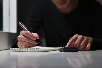 Close up of Asian businessman working on accountant at night while using a calculator for financial. Business and financial concepts.