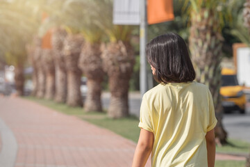 A teenage girl walks along the sidewalk along a row of growing palm trees.