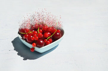 Dissolving magical fruits of cherries and red currants in a heart-shaped vase on a light background. Surreal food concept with free space for text.