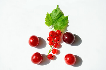 Fruit composition of red currant, cherry and leaf close-up on a textured light background. Minimalistic summer fruit idea with space for text.