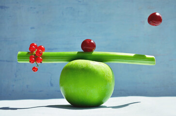 Minimalistic fruit balance composition of summer fruits: apple, red currant, cherry and rhubarb stalk on a blue background. Creative idea of harmony of health and healthy eating.