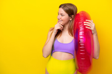 Young caucasian woman holding air mattress isolated on yellow background thinking an idea and...