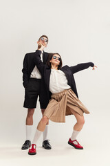 Full-length portrait of stylish young couple, man and woman in retro suit posing isolated over grey studio background. Party mood