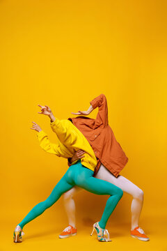Creative colorful portrait of man and woman in bright clothes with hidden faces posing isolated over yellow background. Dancing
