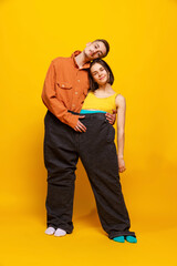 Obraz premium Creative colorful portrait of man and woman in bright clothes, standing together in one pants, hugging isolated over yellow background.
