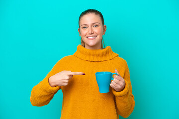 Young caucasian woman holding cup isolated on blue background and pointing it