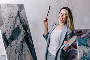 Portrait of female artist. Excited woman paints a picture with a brush.