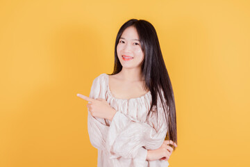Smiling asian woman pointing finger to the side on yellow background