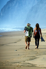 Young couple walking on calm, sandy Cordoama beach with cliffs in background, near Vila Do Bispo,...