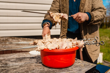 Woman hand impales raw pork meat on a spit from aluminium metal basin, outdoor cooking a poultru shashlik. summer nice day.