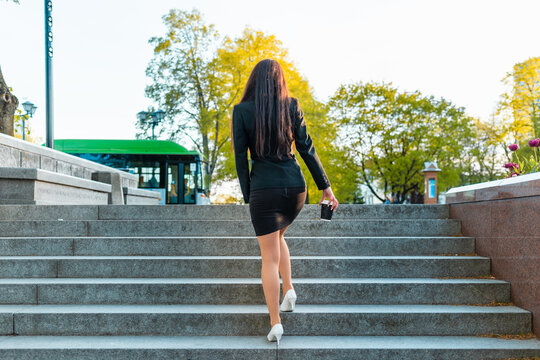 Business woman walking,climb on the stairs holding paper coffee cup,rear view. Caucasian businesswoman wearing a short skirt and going in the city.Rear view.