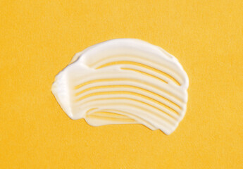 The texture of white cream on yellow background. A smear of moisturizer closeup. Lotion swatch. Beauty, skin care product smear smudge drop. SPF sunscreen cream sample