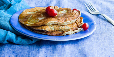 Straight view,close-up of a stack of banana Pancakes with melted butter and cherries as topping. Healthy vegan breakfast concept.Fresh,homemade pancakes in a blue plate on a dark blue background.