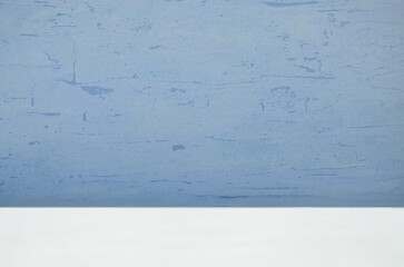 Abstract blurred blue background with stucco texture on the wall and white bottom for product presentation.