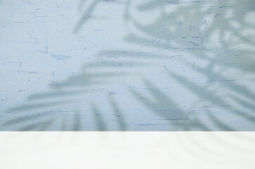Abstract blurred light blue background with stucco texture, palm branch shadow on the wall and white bottom for product presentation.