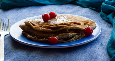 Straight view,close-up of a stack of banana Pancakes with melted butter and cherries as topping. Healthy vegan breakfast concept.Fresh,homemade pancakes in a blue plate on a dark blue background.