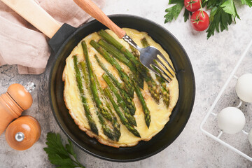 Omelet with asparagus. Frittata or scrambled with asparagus in frying pan with parsley and pepper on gray concrete table background. Useful breakfast concept. Top view.