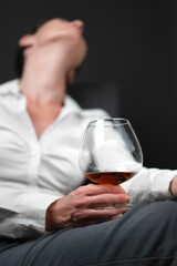 Drinking glass filled with alcohol held by woman in business clothes sitting with her legs crossed...