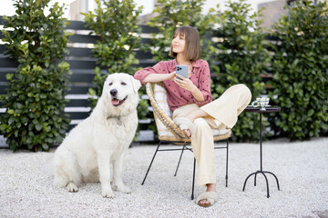 Young woman sitting relaxed with her huge white adorable dog, spending time together at backyard. Friendship with pet and happy leisure time outdoors concept