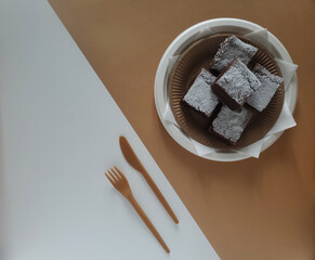 Pieces of chocolate brownie dessert in a plate, fork and knife on brown and white background