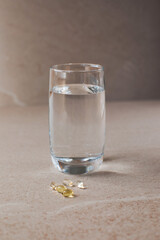 Complex of organic bio supplements, vitamin d, calcium, omega on a beige stone table and a glass of water for health improvement