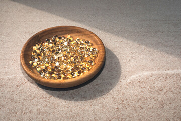 A handful of vegetable vitamin D capsules in a wooden plate on a stone table with sunlight