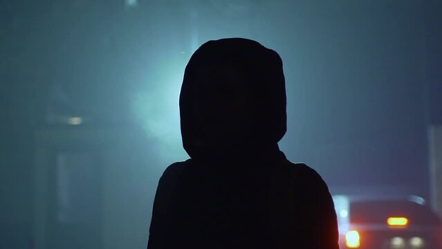 Silhouette of a young man dressed in a hood in the backlight.