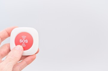 person holding a red SOS button against white background - emergency and danger situation concept