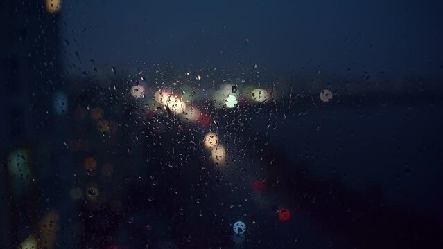 Bokeh of city lights and flashes of lightning through raindrops on the window.