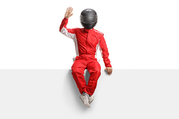 Full length portrait of a racer with a helmet sitting on a blank panel and waving