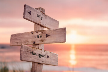 my life changed text quote on wooden crossroad signpost outdoors on beach with pink pastel sunset...