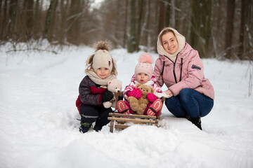 Fototapeta na wymiar Mom and children on a vintage wooden sled against the backdrop of a winter forest. Woman with children on a winter walk.