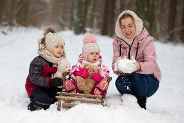 Mom and children on a vintage wooden sled against the backdrop of a winter forest. Woman with children on a winter walk.