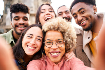 Young multiracial people taking a selfie with smartphone and having fun in the city outdoors.