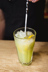 The bartender mixes an alcoholic cocktail in a tall glass with green syrup and ice - cocktail party