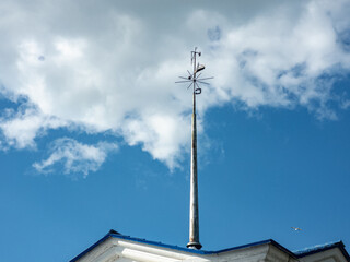 Spire with a shluger on a building against the background of clouds. Weather vane on the roof.