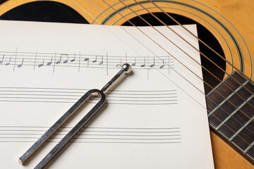 Music recording scene with guitar, music sheets and tuning fork on wooden table, closeup