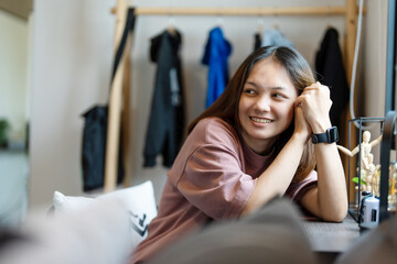 A cute young Asian woman sitting on her bedroom desk smiling happily.