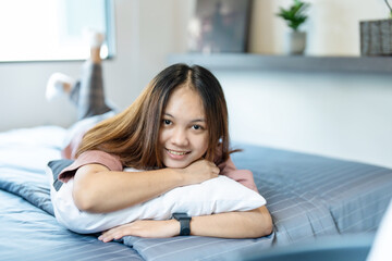 Obraz premium A cute long-haired Asian teenage girl hugging a pillow in bed in her bedroom with a happy smile on her face.