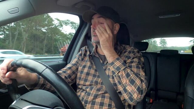 A tired driver rubs his eyes and blinks while driving on a busy highway.