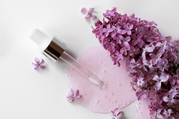 Closeup of pipette with serum, oil, gel with lilac flowers on white background. Skincare, natural beauty products presentation concept. Macro. Romantic floral composition. Front view, high angle shot