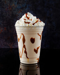 Vanilla milkshake with chocolate syrup in clear glass on dark background.