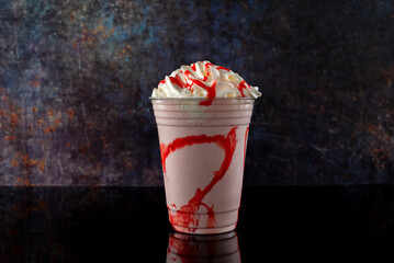 Strawberry milkshake with strawberry syrup in clear glass on dark background.