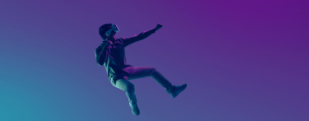 Young Asian man wearing VR headset playing video game and levitating in the air on futuristic...