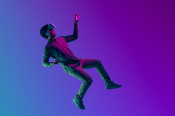 Young Asian man wearing VR headset enjoy playing video game and levitating in the air on futuristic...