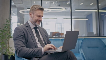 Successful businessman working on laptop, sitting in comfortable office and smiling